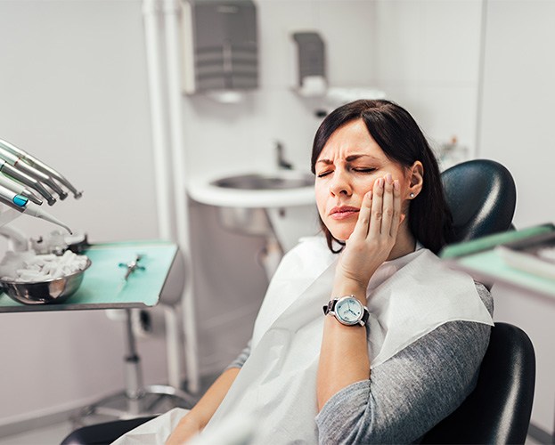 Woman experiencing toothache while sitting in treatment chair